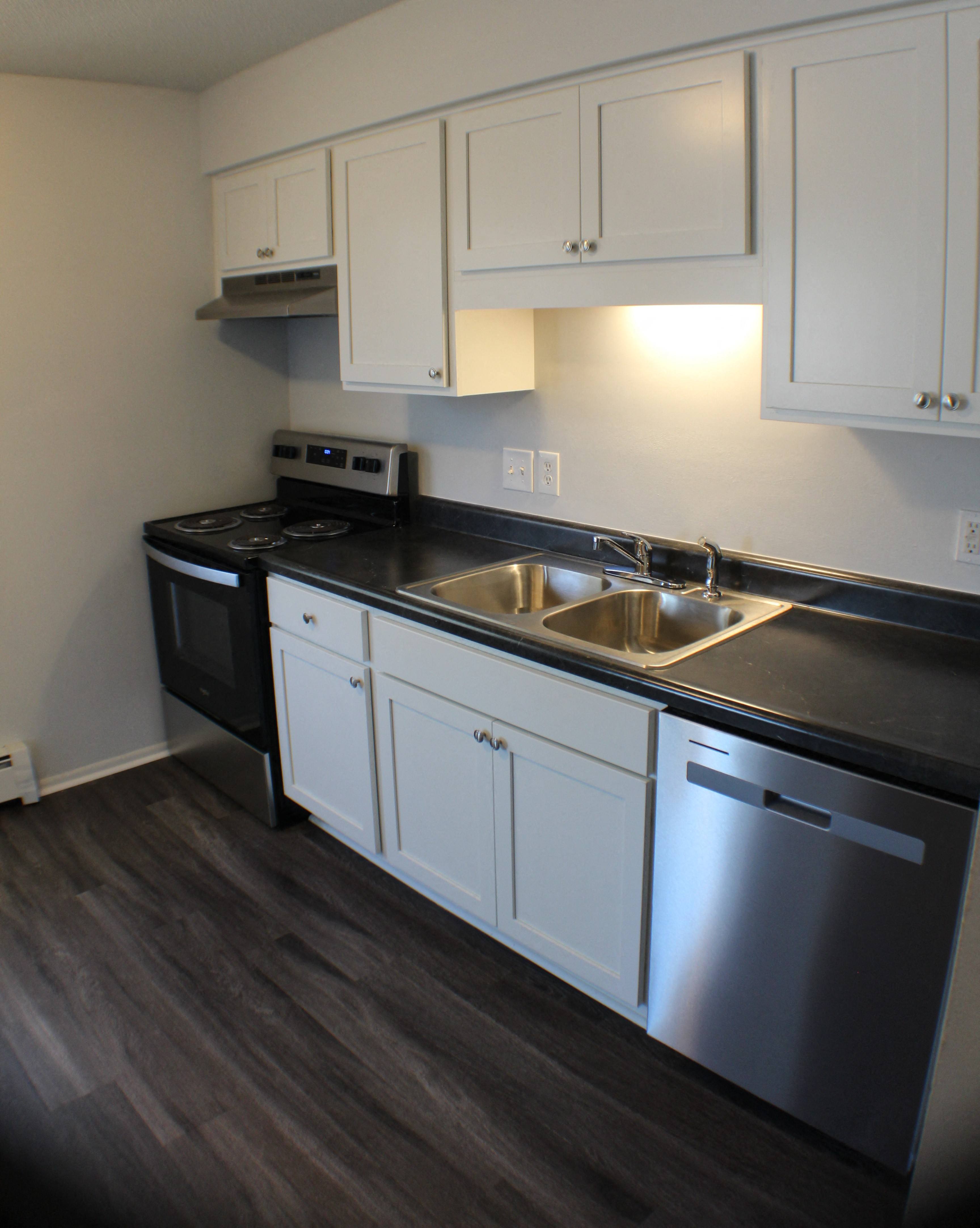 a kitchen with white cabinets and black countertops and a stainless steel sink